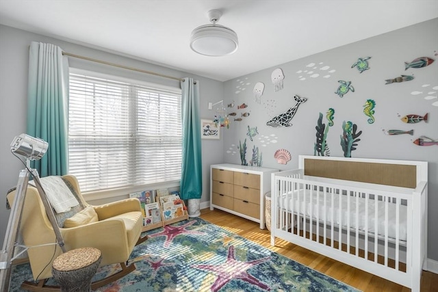 bedroom with baseboards, a nursery area, and wood finished floors
