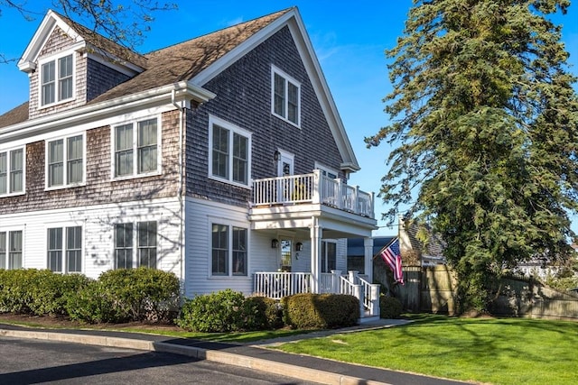 view of front facade with covered porch, a shingled roof, a front lawn, and a balcony