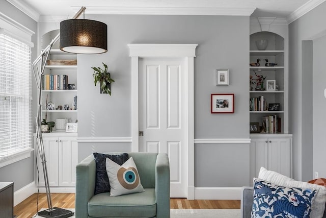 sitting room with crown molding, light wood-style flooring, baseboards, and built in shelves
