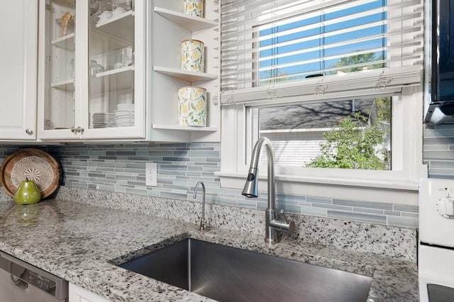 kitchen with backsplash, white cabinetry, light stone countertops, and a sink