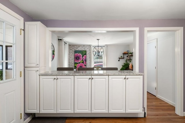 kitchen with pendant lighting, light stone countertops, white cabinetry, and wood finished floors
