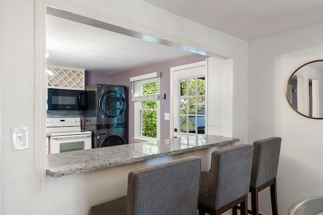 kitchen featuring white range with electric stovetop, black microwave, stone counters, and stacked washer and clothes dryer