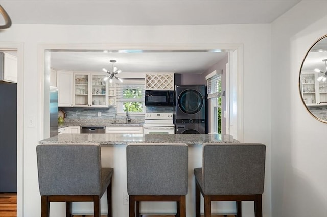 kitchen featuring stacked washer / drying machine, white electric range oven, black microwave, a sink, and an inviting chandelier