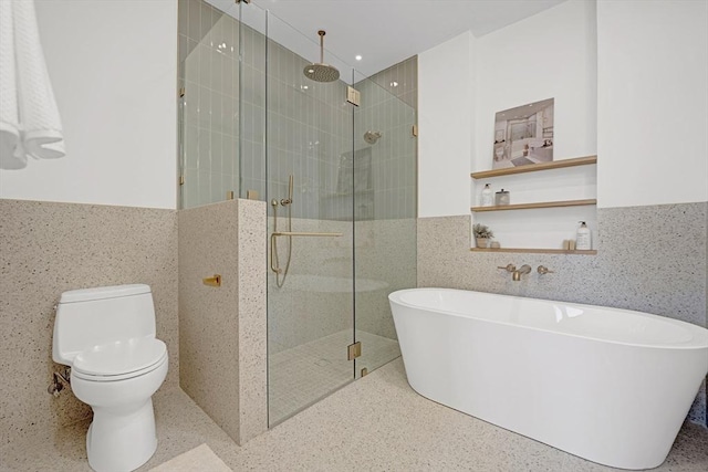 full bath with wainscoting, toilet, a freestanding bath, a shower stall, and tile walls