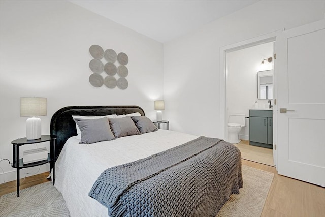 bedroom with baseboards, connected bathroom, and light wood finished floors