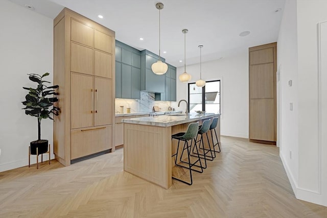 kitchen with light brown cabinets, a sink, a kitchen breakfast bar, light countertops, and a center island with sink