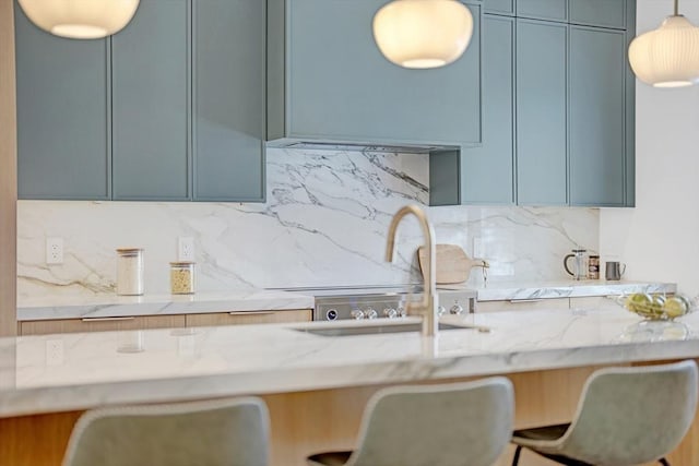 kitchen featuring light stone counters, decorative light fixtures, a sink, and backsplash