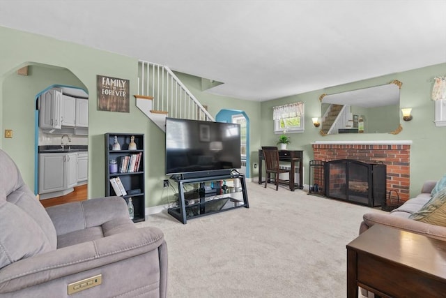 48 Gorham Ave, Stoneham, MA 02180 - carpeted living area featuring arched walkways, a fireplace, stairs, a sink, and baseboards
