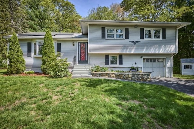 split level home featuring asphalt driveway, an attached garage, and a front lawn