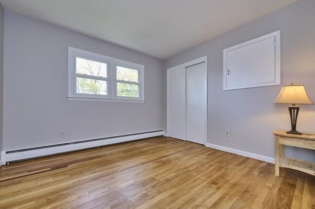 unfurnished bedroom featuring a baseboard heating unit, wood finished floors, baseboards, and a closet