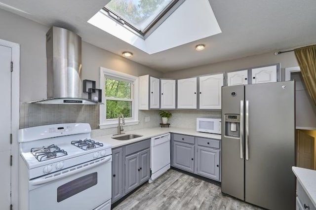 kitchen featuring white appliances, a sink, gray cabinets, wall chimney range hood, and a skylight