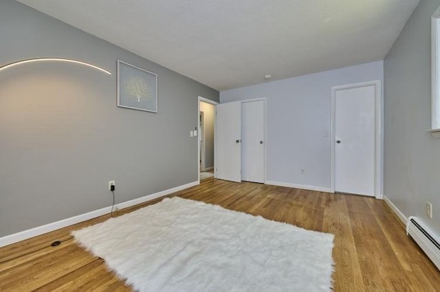 unfurnished bedroom with a baseboard heating unit, wood finished floors, and baseboards