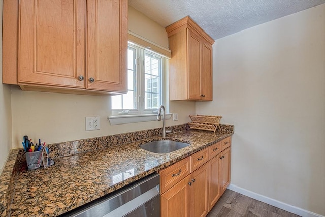 kitchen with wood finished floors, baseboards, dark stone counters, a sink, and a textured ceiling