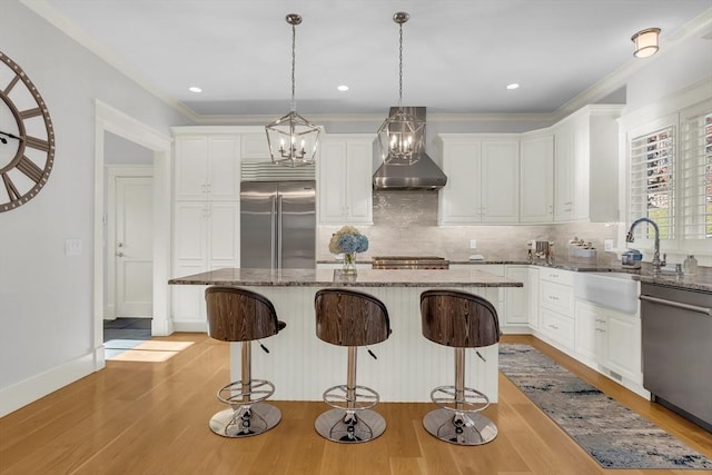 kitchen featuring light wood-style flooring, decorative backsplash, stainless steel appliances, a sink, and wall chimney exhaust hood