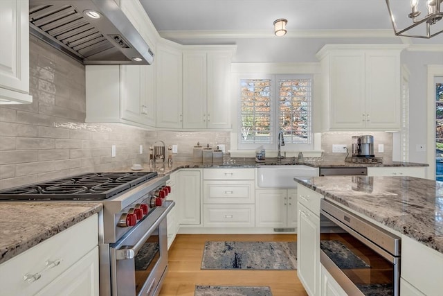 kitchen with white cabinetry, wall chimney exhaust hood, appliances with stainless steel finishes, and a sink