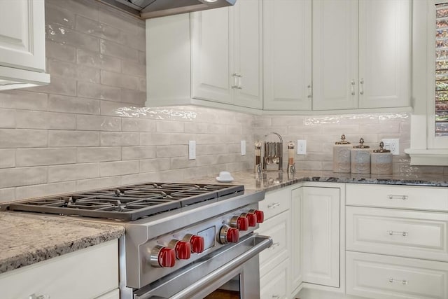 kitchen with white cabinetry, tasteful backsplash, high end stove, and light stone counters