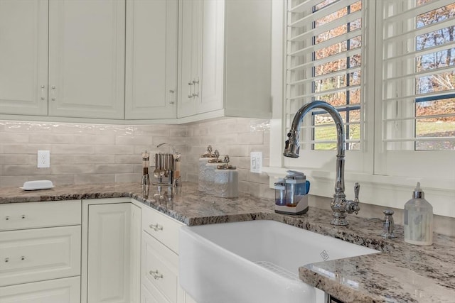 kitchen with white cabinets, backsplash, stone counters, and a sink