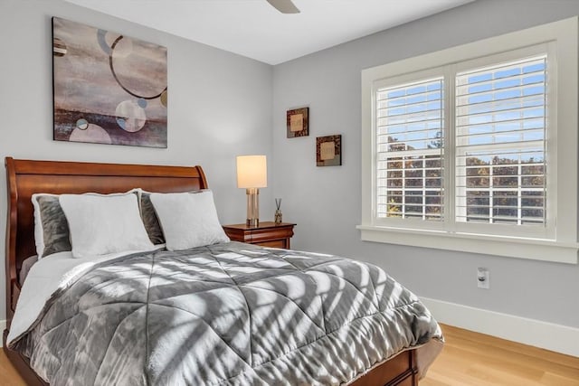 bedroom featuring baseboards, wood finished floors, a ceiling fan, and multiple windows