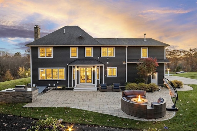 rear view of property featuring a chimney, an outdoor fire pit, a patio, french doors, and a lawn