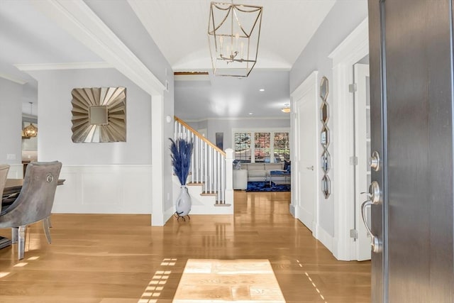 foyer entrance with wood finished floors, an inviting chandelier, stairs, crown molding, and lofted ceiling