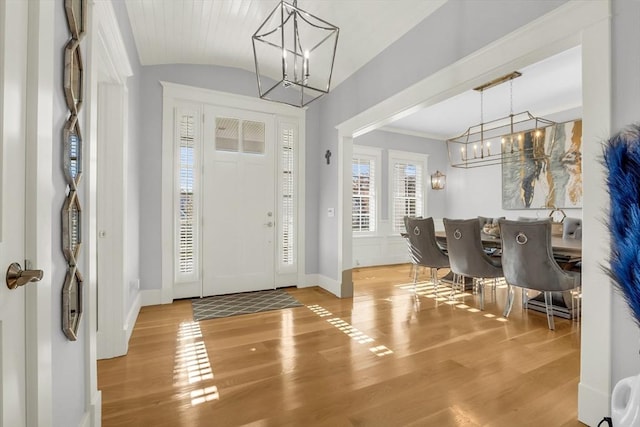 foyer entrance with wood finished floors, a chandelier, vaulted ceiling, and baseboards