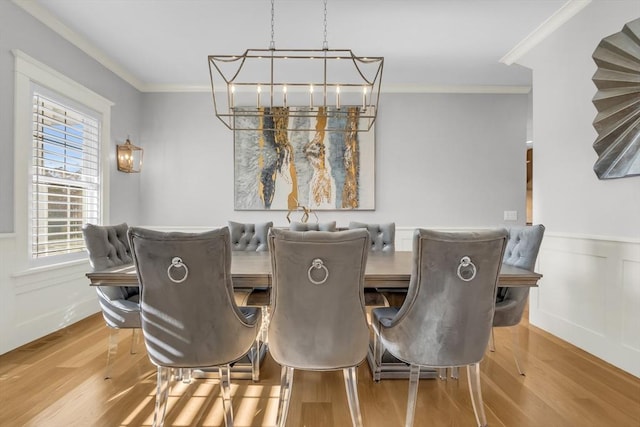 dining space with ornamental molding, a wainscoted wall, a decorative wall, and wood finished floors