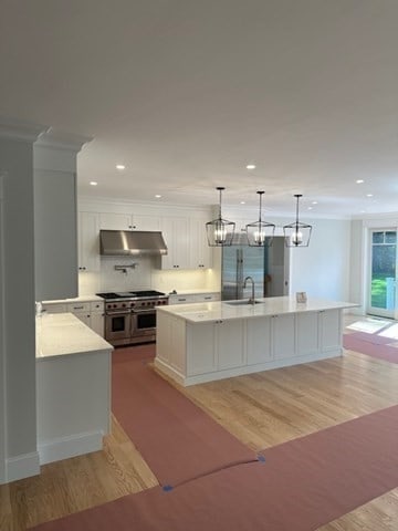 kitchen featuring pendant lighting, double oven range, a large island with sink, white cabinets, and light wood-type flooring