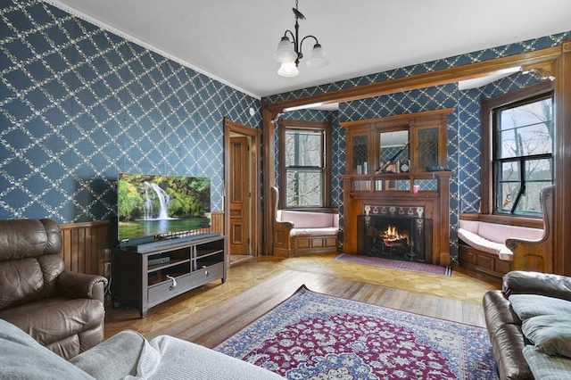 living area featuring a notable chandelier, a warm lit fireplace, wood finished floors, and wallpapered walls