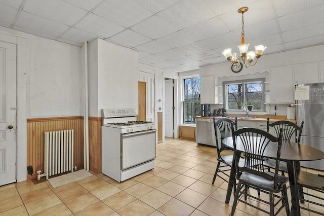 kitchen featuring radiator heating unit, wainscoting, a notable chandelier, stainless steel appliances, and a paneled ceiling