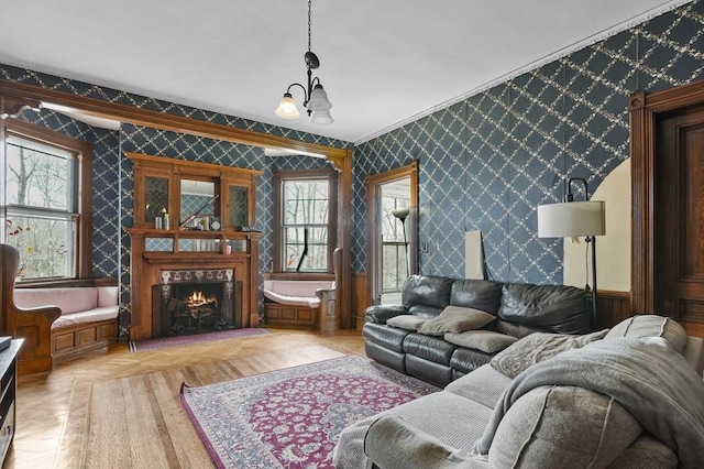 living room with a healthy amount of sunlight, a warm lit fireplace, wallpapered walls, and an inviting chandelier