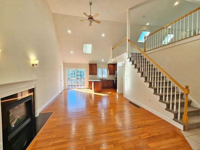 unfurnished living room featuring light wood-type flooring, high vaulted ceiling, and ceiling fan