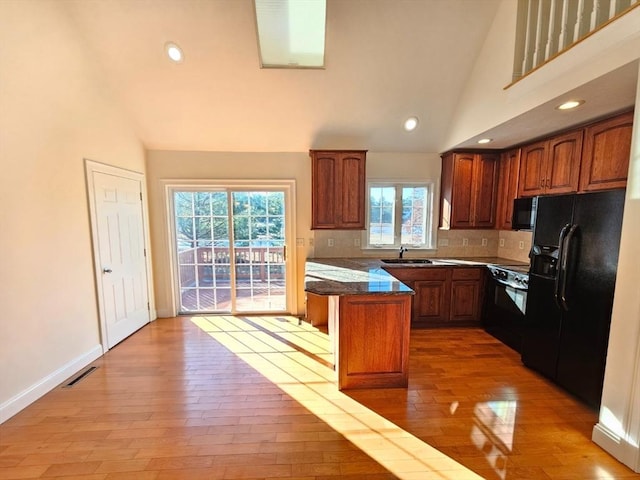 kitchen featuring light wood-type flooring, a center island, vaulted ceiling, and black appliances