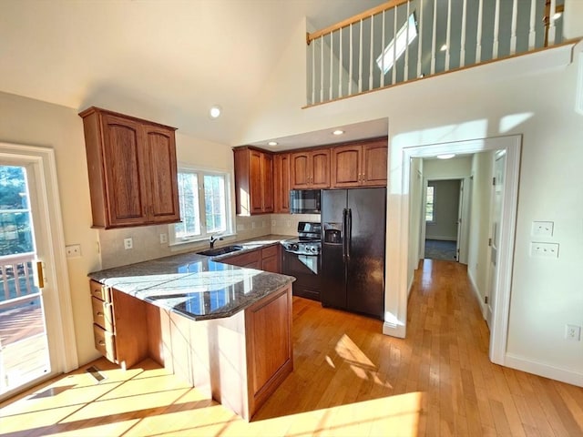 kitchen featuring sink, tasteful backsplash, kitchen peninsula, dark stone counters, and black appliances