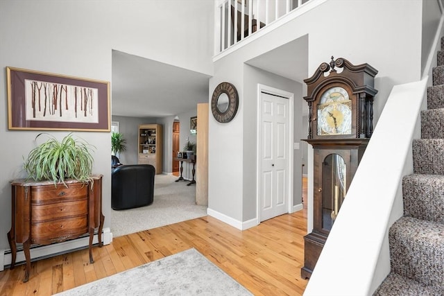 stairs with a high ceiling, wood-type flooring, and a baseboard radiator