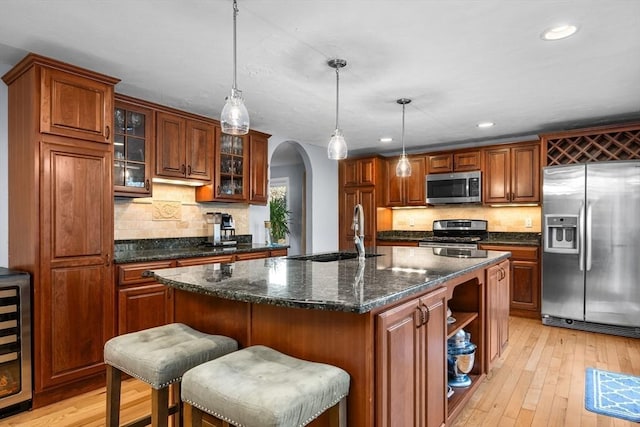 kitchen with sink, hanging light fixtures, light hardwood / wood-style flooring, a kitchen island with sink, and appliances with stainless steel finishes