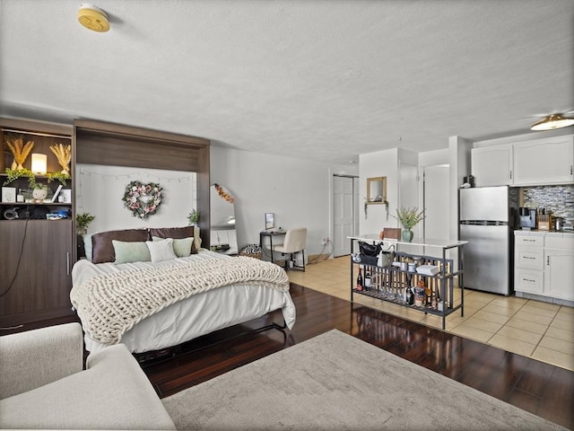 bedroom with freestanding refrigerator, a closet, a textured ceiling, and light wood-style flooring