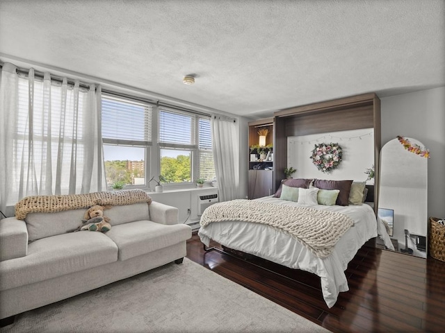 bedroom featuring a textured ceiling, wood finished floors, and a wall unit AC