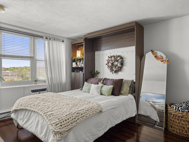 bedroom with baseboard heating, a wall mounted air conditioner, a textured ceiling, and wood finished floors
