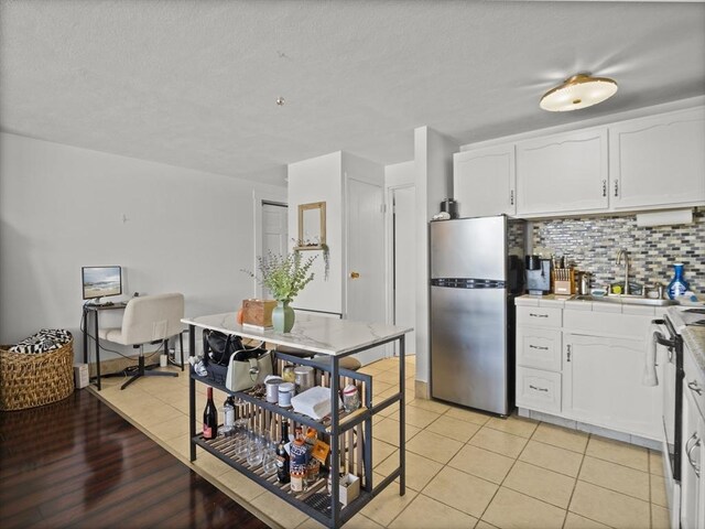kitchen with a sink, freestanding refrigerator, white cabinets, backsplash, and electric range
