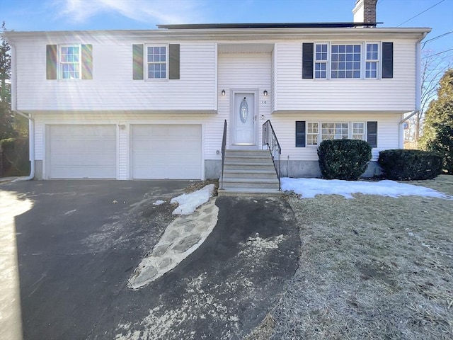 raised ranch featuring aphalt driveway, an attached garage, and a chimney