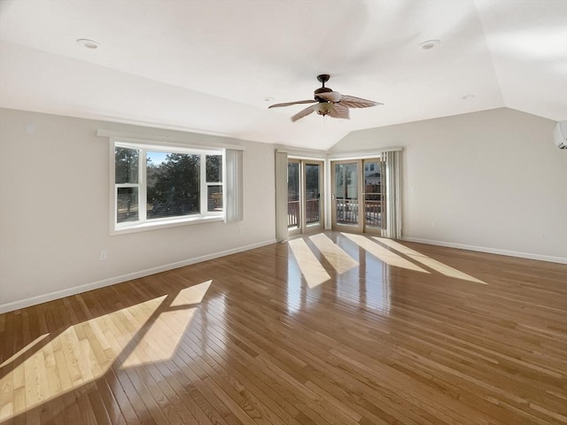 spare room featuring a wall unit AC, wood-type flooring, baseboards, and vaulted ceiling