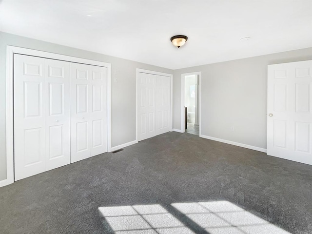 unfurnished bedroom with baseboards, carpet floors, visible vents, and multiple closets