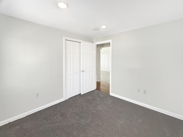 unfurnished bedroom with dark colored carpet, a closet, baseboards, and recessed lighting