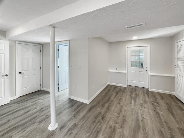 below grade area featuring visible vents, a textured ceiling, baseboards, and wood finished floors