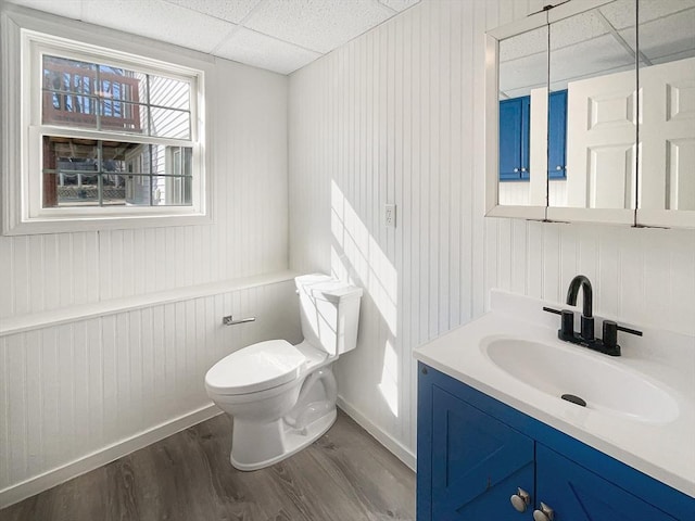 bathroom with vanity, wood finished floors, baseboards, a drop ceiling, and toilet