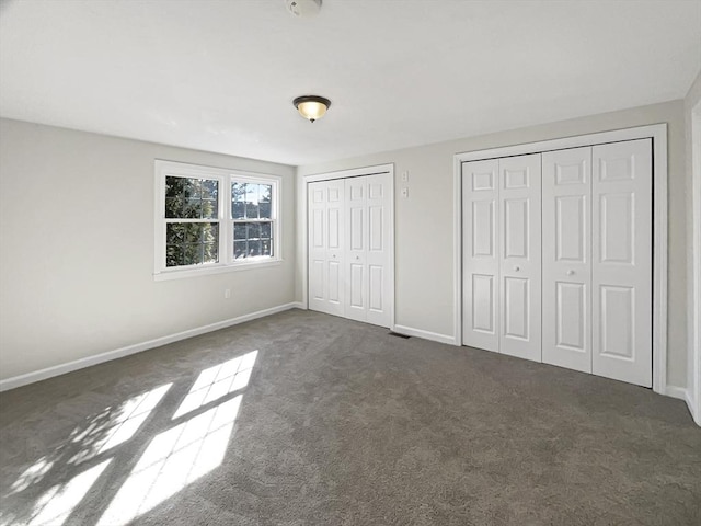 unfurnished bedroom with baseboards, multiple closets, and dark carpet