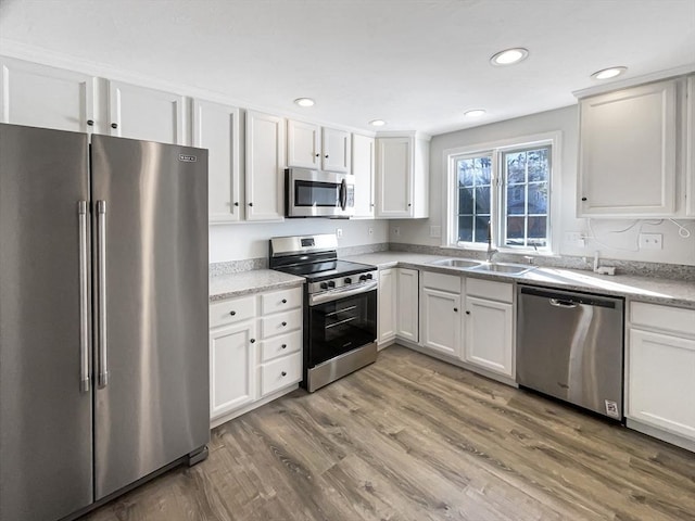 kitchen with white cabinets, stainless steel appliances, light wood-type flooring, and a sink