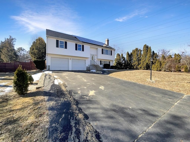 bi-level home featuring aphalt driveway, roof mounted solar panels, a garage, and fence