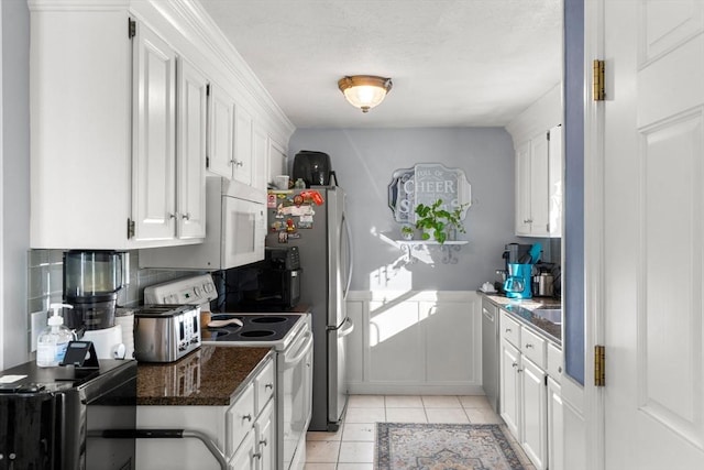 kitchen featuring white cabinetry, dark stone counters, light tile patterned floors, white appliances, and a healthy amount of sunlight