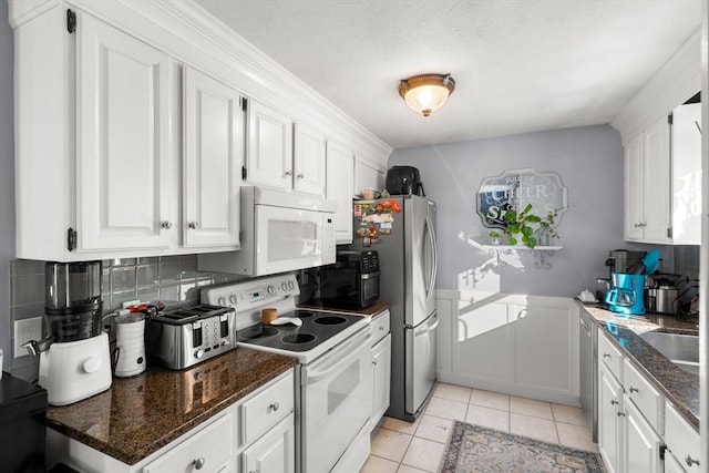 kitchen featuring white cabinetry, tasteful backsplash, light tile patterned floors, white appliances, and dark stone countertops